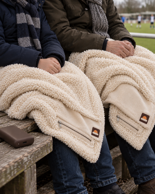 Twee mensen op de tribune, elk onder een crème WARMDEK warmtedeken